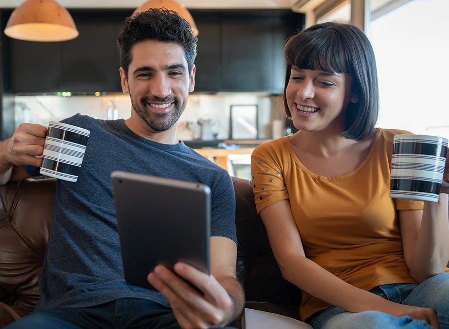 Casal sorrindo no sofá enquanto usa um tablet